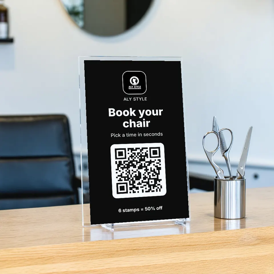 A "Book your chair" sign for ALY STYLE on a barbershop counter